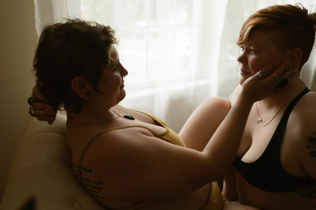 two women sitting in front of a window, one is touching the other's face gently | Virginia Boudoir Photographer