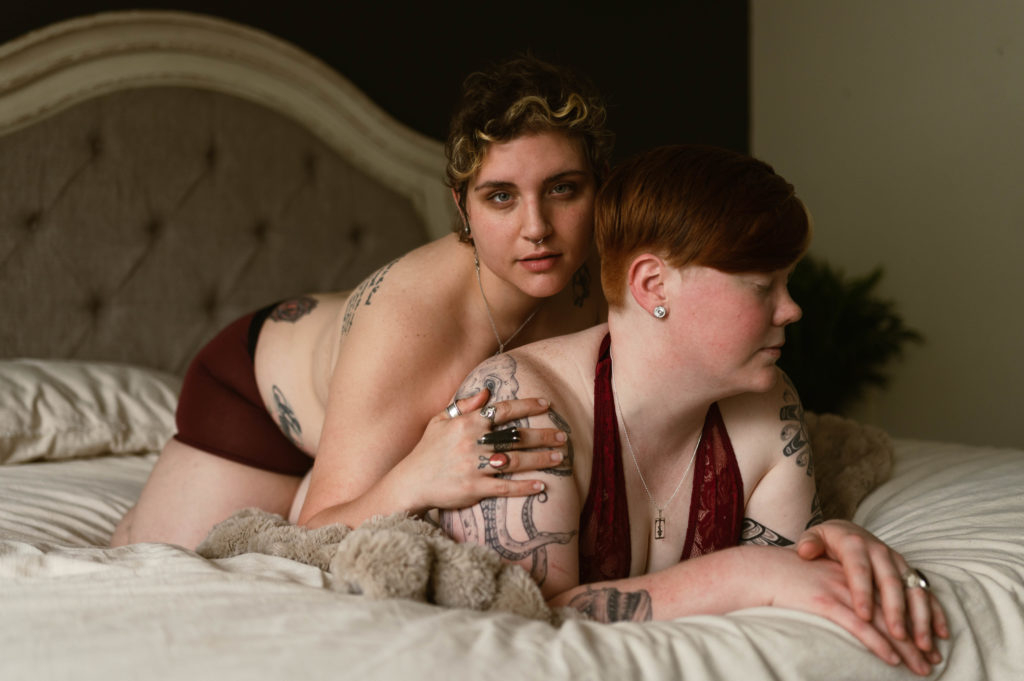 Two women lying on top of each other on the bed, both in red lingerie. | Virginia Sensual Photography