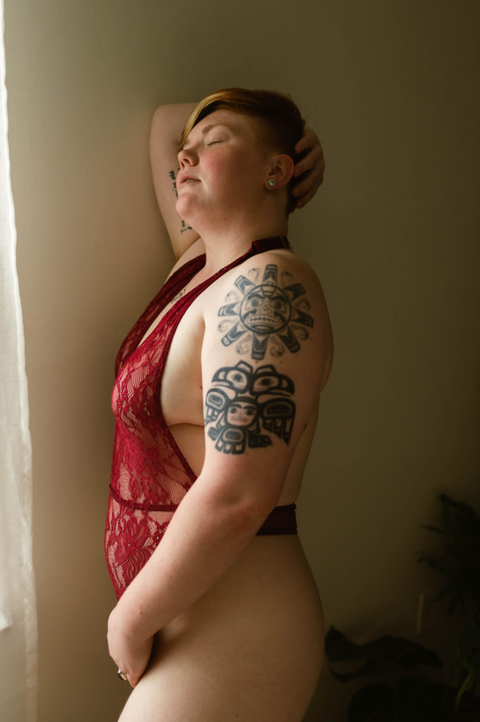 Photo of woman with short hair in red lace lingerie by a window, eyes closed. | Virginia Sensual Photography