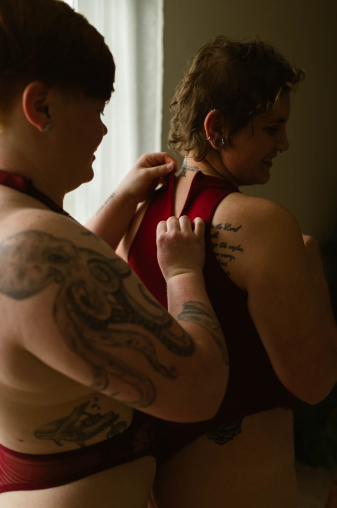 Photo of a short haired woman getting her lingerie zipped up by her partner by a window. | Virginia Sensual Portrait Photography.