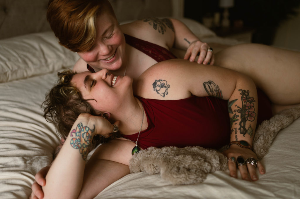 Couple in red lingerie laughing on a bed together in their sensual lifestyle photo session