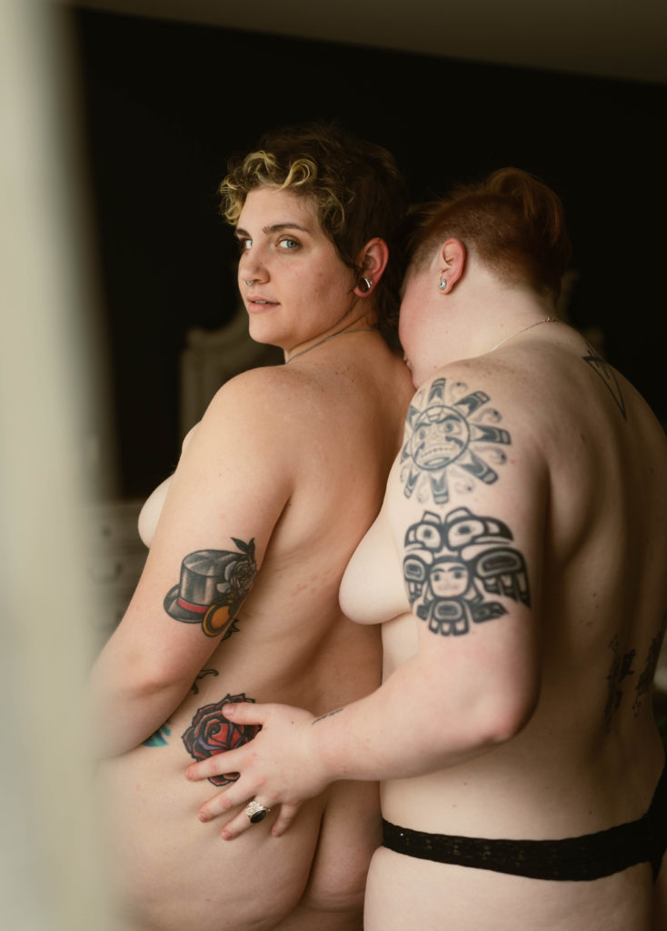 Two topless women embracing, facing away from the camera. Woman with short hair looking back at the camera. | Virginia Sensual Photography