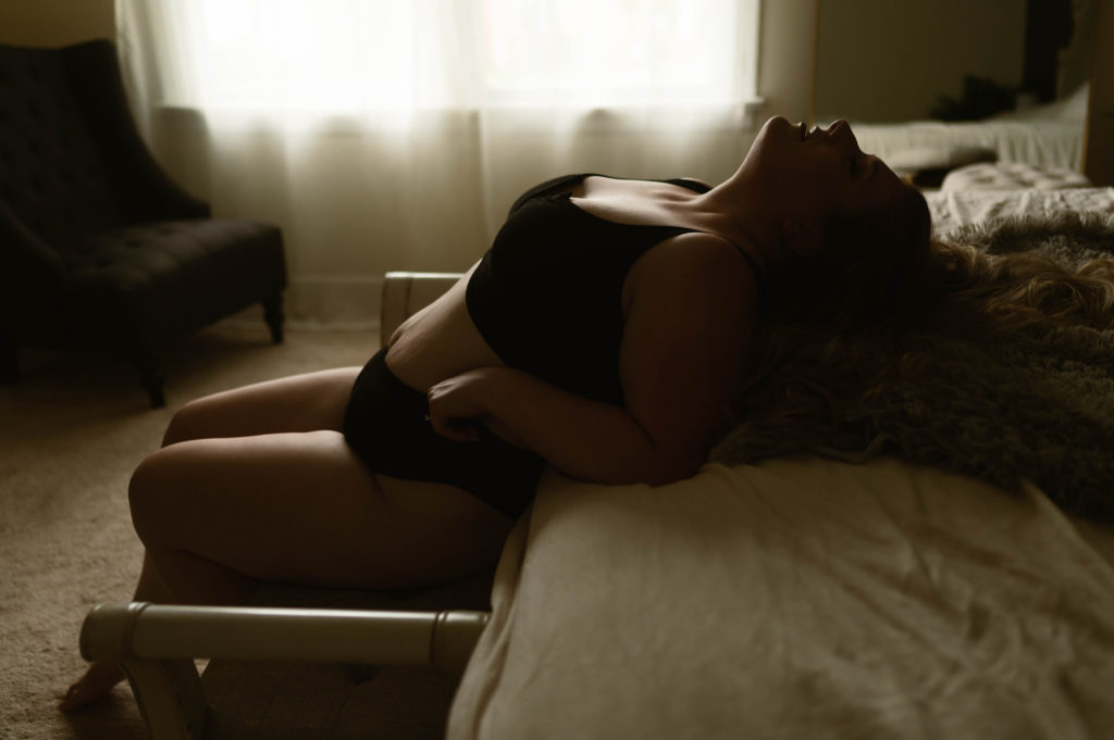 Woman in matching black lingerie leaning back against the bed. 