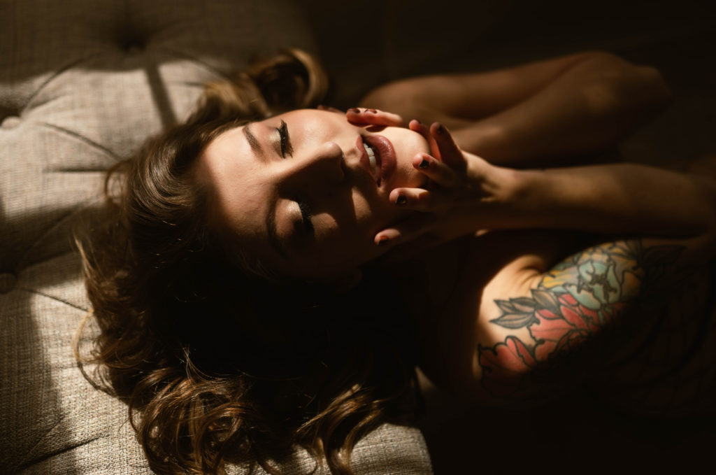 Close up boudoir image of a woman with tattoos, with her hands on her face, eyes closed. 