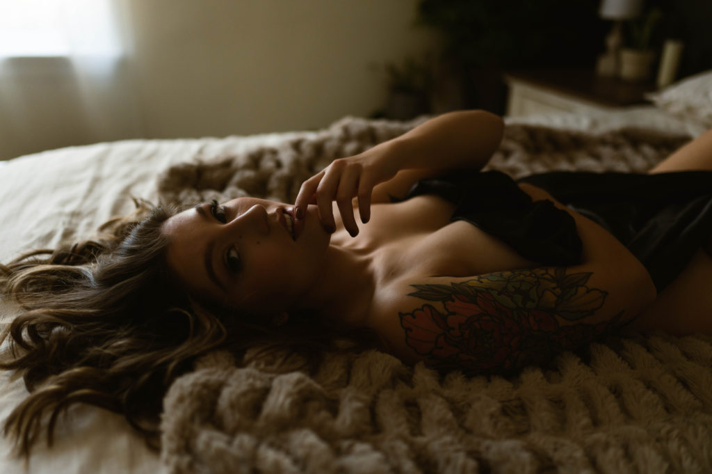 Woman lying on a bed, covered by only a sheet, looking at camera.