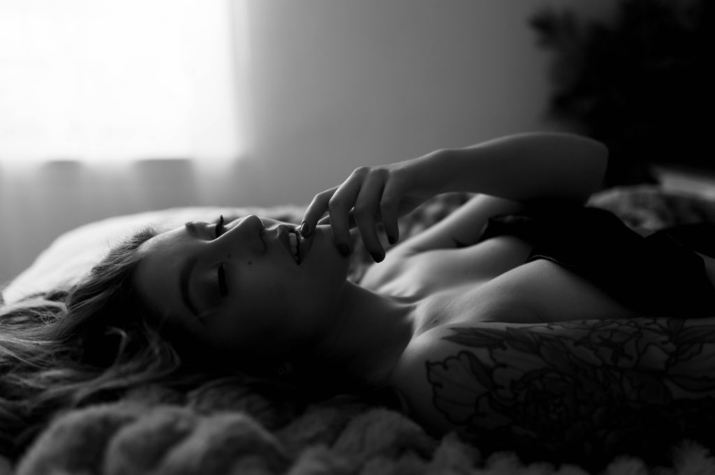 Sexy black and white photo of woman on bed, finger against her lips.