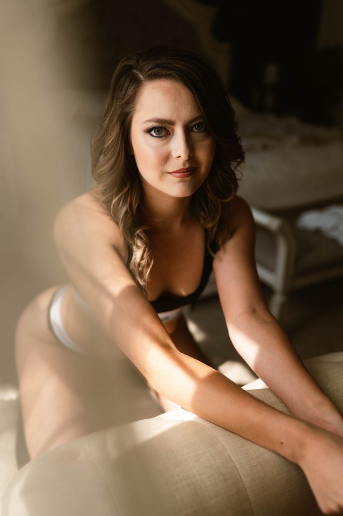 Photo of a brunette woman at her sensual photo session. She is kneeling on a chair, hands over the back of the chair, looking into camera | Virginia Boudoir Photographer