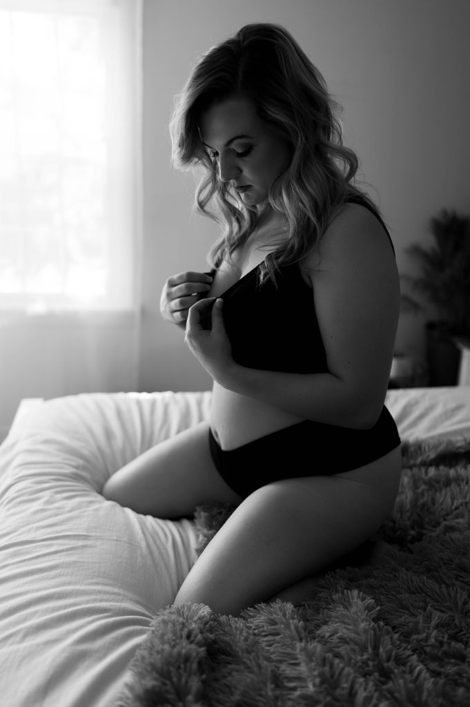 Black and white photo of a woman in black two piece underwear set, kneeling on a bed at her boudoir session in Virginia.