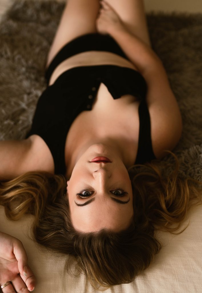 Blonde woman lying on her back, eyes looking up and back into the camera.