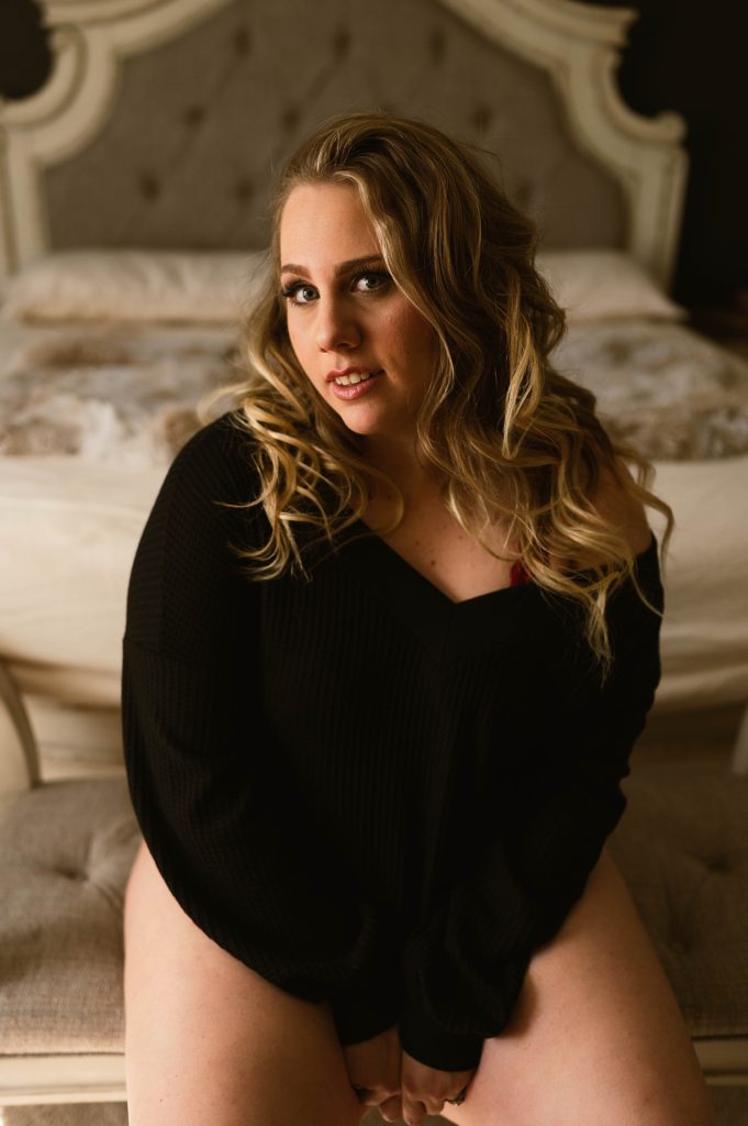 Blonde woman looking at the camera in a black sweater and no pants.