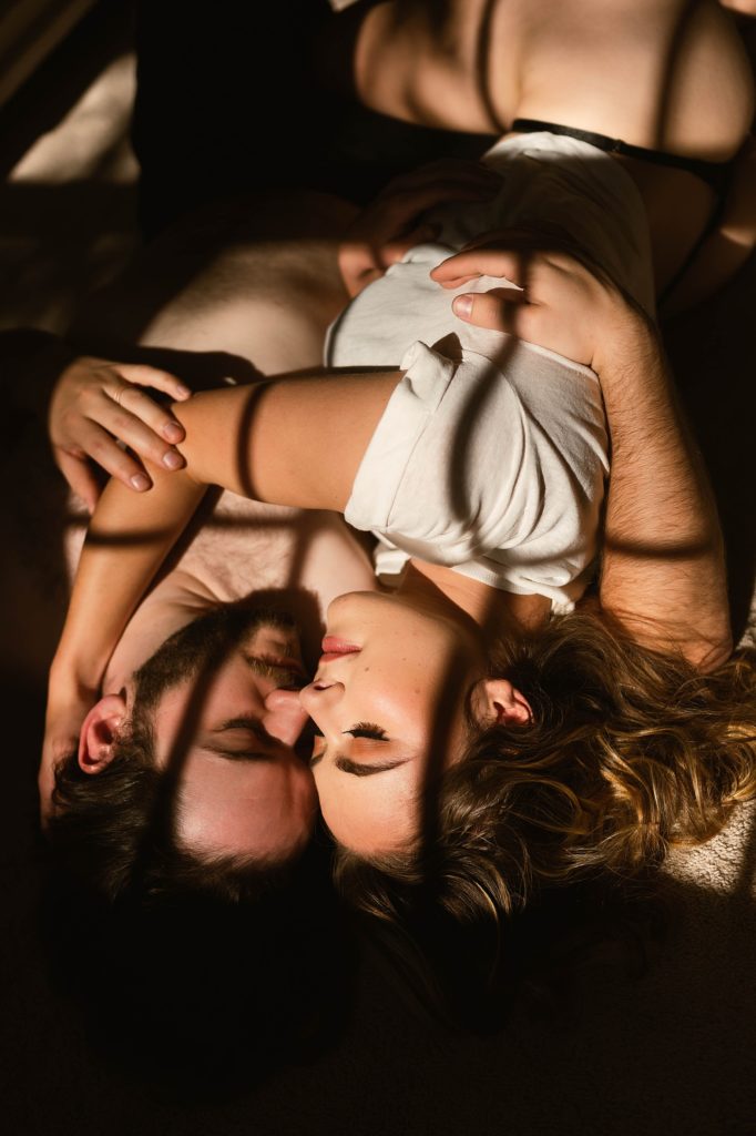 Couple embracing in very little clothing with shadows from the window pane falling over them. 