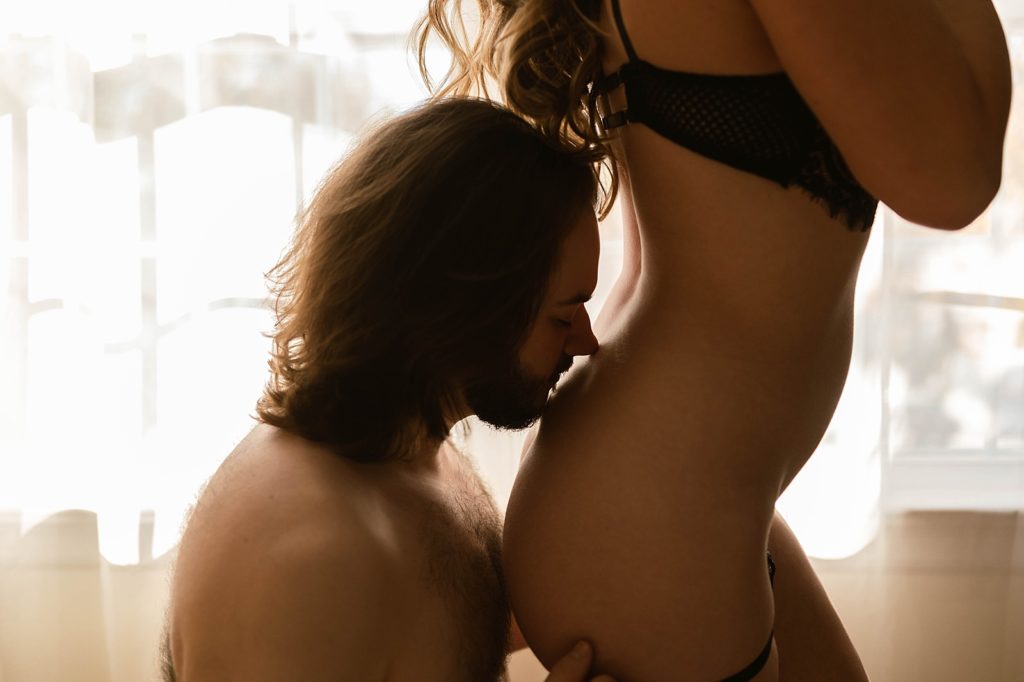 Man kissing woman in lingerie's lower back.