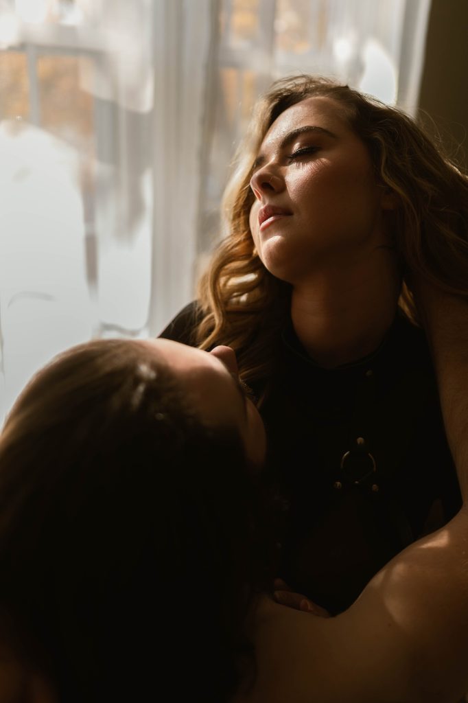 Woman and man embracing sensually next to a window.