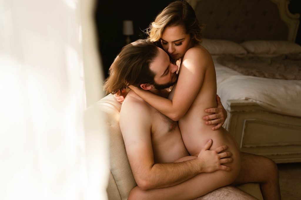 Nude man and woman sitting on a chair together for their couples boudoir session.