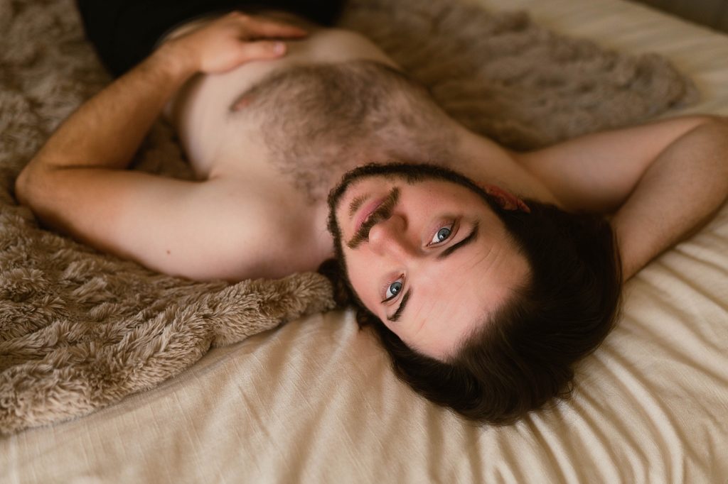 Shirtless man looking back at the camera while he lies on the bed.