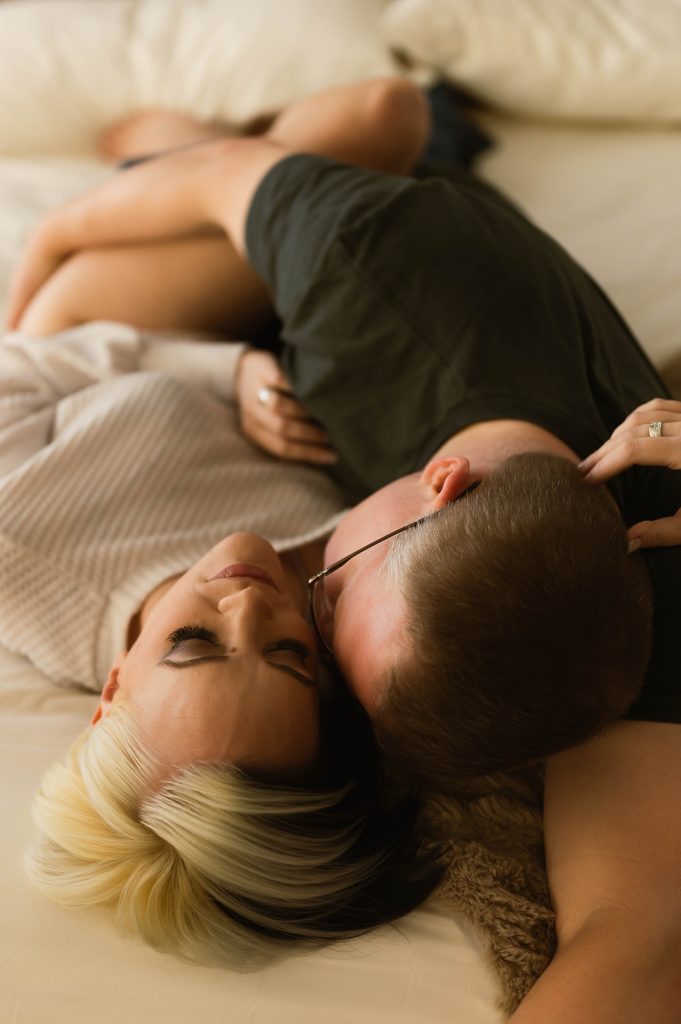 A couple in sweaters curled up on a bed for their couples boudoir session in Virginia. 