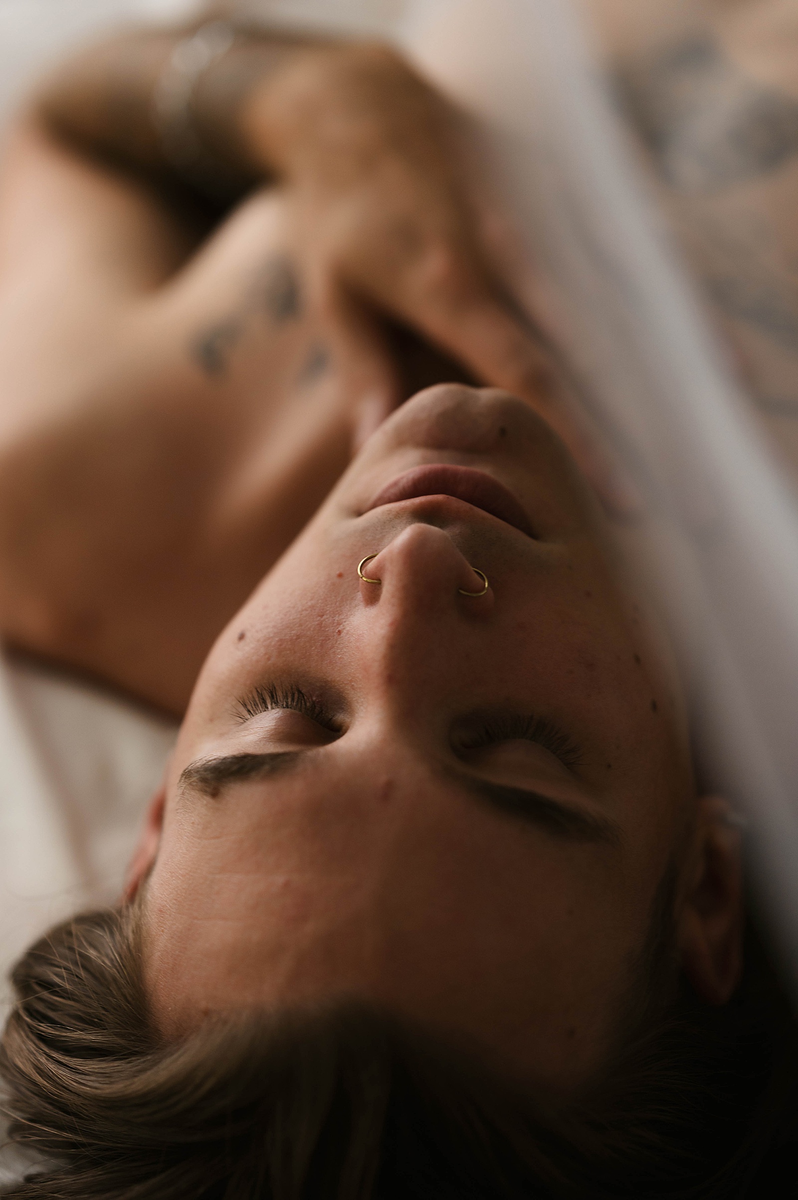 Man with nose rings lying on a bed for a boudoir shoot 